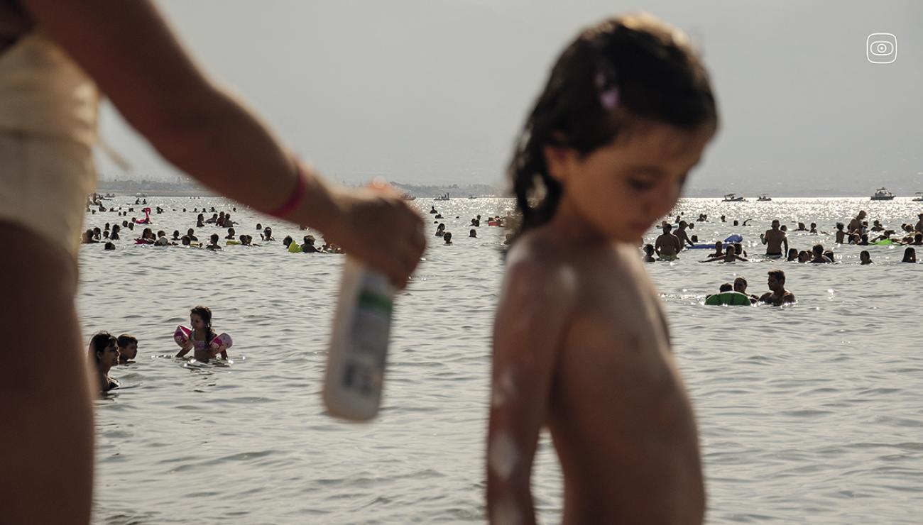 Beachgoers lather on sunscreen while bathing along the Mediterranean shoreline in Palermo, Sicily