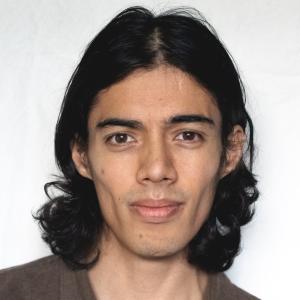 A young skinny man with curly black hair reaching his shoulders