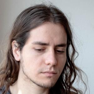 Jordi Jon - a young man with dark shoulder-length hair, not looking directly into the camera