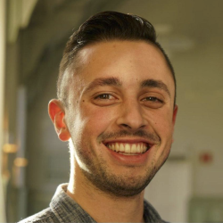 A young man with short dark hair stares smilingly into the camera