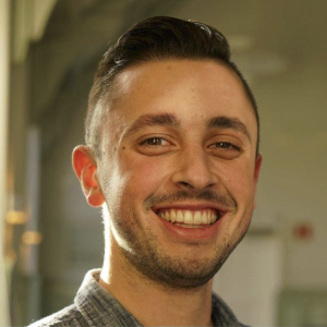 A young man with short dark hair stares smilingly into the camera