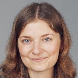 A young woman with big soft curls od dark goden colour and blue eyes smiles into the camera