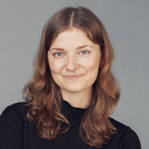 A young woman with big soft curls od dark goden colour and blue eyes smiles into the camera