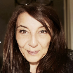 A woman with striaght dark hair and reading glasses o top of her head stares intensely into the camera