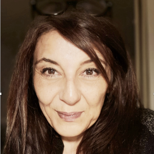 A woman with striaght dark hair and reading glasses o top of her head stares intensely into the camera