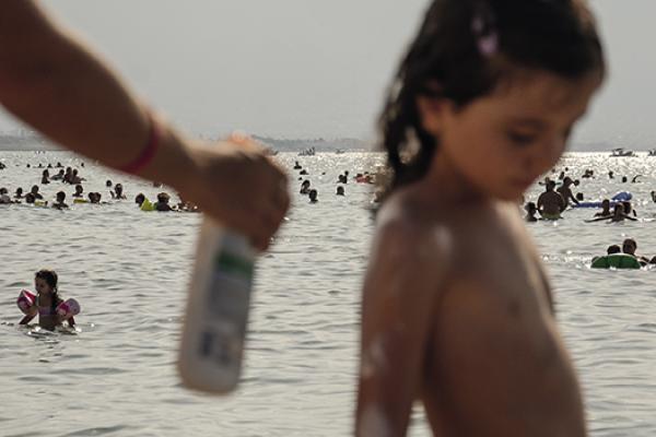 Beachgoers lather on sunscreen while bathing along the Mediterranean shoreline in Palermo, Sicily