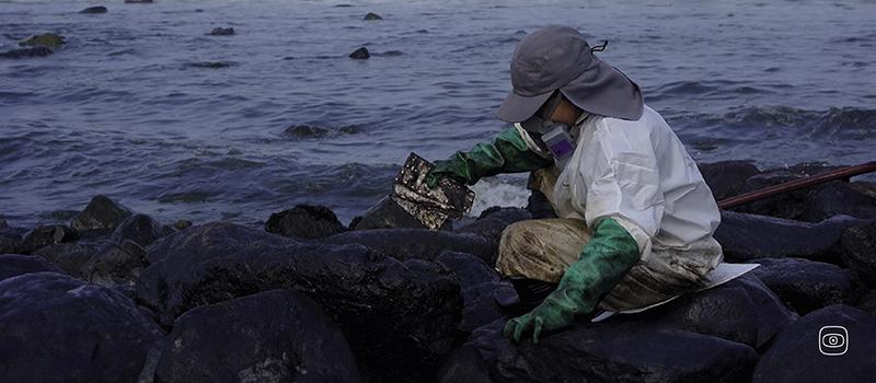 a person in protective gear cleaning the crude oil spill on the seashore